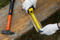 Close up of carpenter hand wearing working gloves and measuring plank with a tape measure Royalty Free Stock Photo