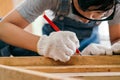 Close-up carpenter hands wearing work gloves draw the cutting line with a pencil on a wooden board. Construction industry, Royalty Free Stock Photo