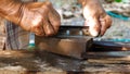 Close up carpenter old man hands sharpen blade knife of planer tool with whetstone in rural nature background.