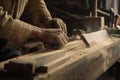 Close-up of a carpenter\'s hands in work clothes sawing a wooden board, with various tools and sawdust on the table