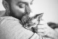 Close-up of cat and man. Portrait of a Devon Rex kitten and young beard guy. Handsome animal-lover man is hugging and cuddling his