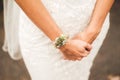 Close up of caucasian bride`s hands with floral bracelet over white lace wedding gown. Wedding day concept. Royalty Free Stock Photo
