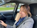Close up of Caucasian businesswoman driving car in city looking at road with big opened eyes holding coffee in mouth Royalty Free Stock Photo