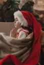 Close-up Caucasian child, lovely baby girl in Santa hat, makes cherished wish and cute presents, surrounded by Christmas Royalty Free Stock Photo