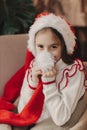 Close-up Caucasian child, lovely baby girl in Santa hat, makes cherished wish and cute presents, surrounded by Christmas