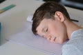 Close-up of caucasian elementary schoolboy sleeping on book at desk in classroom Royalty Free Stock Photo