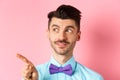 Close-up of caucasian male model with moustache and bow-tie, looking and pointing left with intrigued smile, showing