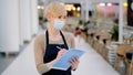 Close-up caucasian middle-aged woman cafeteria restaurant worker waitress in medic face mask writing with pen receiving