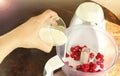 Close-up of a Caucasian woman`s hand pours milk from a glass into a food processor for making a raspberry milkshake.