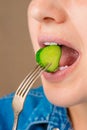 Close-up of a Caucasian woman's mouth as she bites a small piece of fresh cucumber that she holds on a fork.