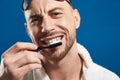 Close up of Caucasian young man brushing his teeth against blue background Royalty Free Stock Photo