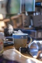 a ceramic cup of hot smoke coffee on wooden table with blurred coffee machine in background