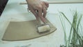 Close up ceramist hands imprinting herb on raw clay with rolling pin. Handmade, hobby art and handicraft concept