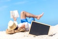 Close up of a chalkboard on the sand of a beach, background happy smiling caucasian tourist asian young man relax and reading book Royalty Free Stock Photo