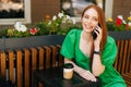 Close-up of charming smiling young woman talking by mobile phone sitting at table with coffee cup in outdoor cafe Royalty Free Stock Photo