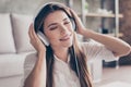 Close up of charming young lady in big modern headphones. She is dreamy and happy, listening to her favourite song, holding the ea