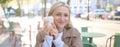 Close up of cheerful blond woman, holding cup of coffee, drinking tea in street outdoor cafe, smiling with happy face Royalty Free Stock Photo