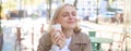 Close up of cheerful blond woman, holding cup of coffee, drinking tea in street outdoor cafe, smiling with happy face Royalty Free Stock Photo