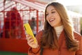 Close-up of cheerful girl in puffer jacket using smartphone outdoor