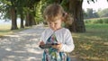 CLOSE UP: Cheerful little daughter with brown hair listens to music on her parent`s cell phone while walking in the park.