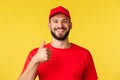 Close-up of cheerful, optimistic bearded employee, courier in red uniform, show thumbs-up, encourage clients order