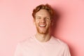 Close up of cheerful young man with messy red hair and beard, laughing and smiling, showing white teeth, looking happy Royalty Free Stock Photo