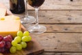 Close-up of cheese with grapes on wooden board by wineglasses on table, copy space