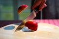 Close up of chef hand chopping apple in half with kitchen knife on the table. Slicing red apple on wooden board Royalty Free Stock Photo