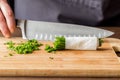 A chef holding a sharp knife in behind a bundle and pile of fresh chives.