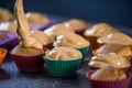 Close up chef pastry is pouring cream on freshly prepared cupcakes on dark background. Concept of confectionery cooking