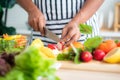 Close-up of chef`s hand using stainless steel knife to cut radishes on a wooden cutting board