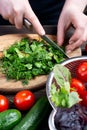 Close up of the chef`s hands cutting parsley and dill on an oval wooden Board surrounded by fresh vegetables on a wooden table Royalty Free Stock Photo