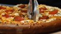 Close-up of chef in white gloves using a pizza cutter slicing delicious pizza with salami, cheese and pickled cucumbers Royalty Free Stock Photo