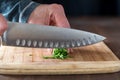 Close up of a chef& x27;s hands cutting a bundle of chives on a wooden board.