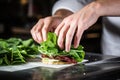 close-up of a chefs hand placing a fresh leaf of lettuce onto a sandwich