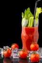 Close-up of cherry tomatoes with ice, bloody mary cocktail with celery and black straw, with selective focus, on wet slate and bla