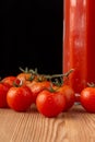 Close-up of cherry tomatoes on wood with bottle of tomato juice, black background, vertical,