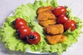 Chicken nagets in breadcrumbs on green lettuce leaves with tomatoes in a white plate. Close-up. Royalty Free Stock Photo