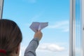 Close-up, a child girl, launches a paper plane from the window, against the sky, there is a place for the inscription