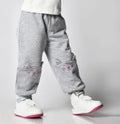 Close-up of a child in gray sports pants with a print of a cat's face and white sneakers on a gray background Royalty Free Stock Photo