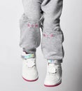 Close-up of a child in gray sports pants with a print of a cat& x27;s face and white sneakers on a gray background Royalty Free Stock Photo