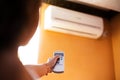 Close-up of child hand adjusting air conditioner with remote control on orange background. Royalty Free Stock Photo