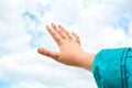 Close up of child hand raised up over blue sky and clouds background. Gesture Royalty Free Stock Photo