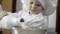 close up of child pour a milk bottle into steel bowl. Young boy with chef uniform cooks in the kitchen with his father