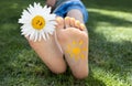 close-up of child\'s bare feet on green grass on sunny day. smiling daisy flower between toes Royalty Free Stock Photo