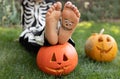 close-up of child\'s bare feet with grin drawn on in black paint and eyes, two carved orange pumpkins