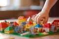 Close-up of a child\'s hand assembling colorful building blocks to create a miniature town