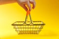 Close up of child`s hand holds handles metal grocery basket for shopping in supermarket with orange plastic elements