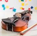 Close up of a child violin and bow, lying on a white desk with blurred white board background with colorful letters and numbers.