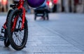 Close up children bicycle parked on the road in town. Red bicycle with black wheels. Kid`s bicycle